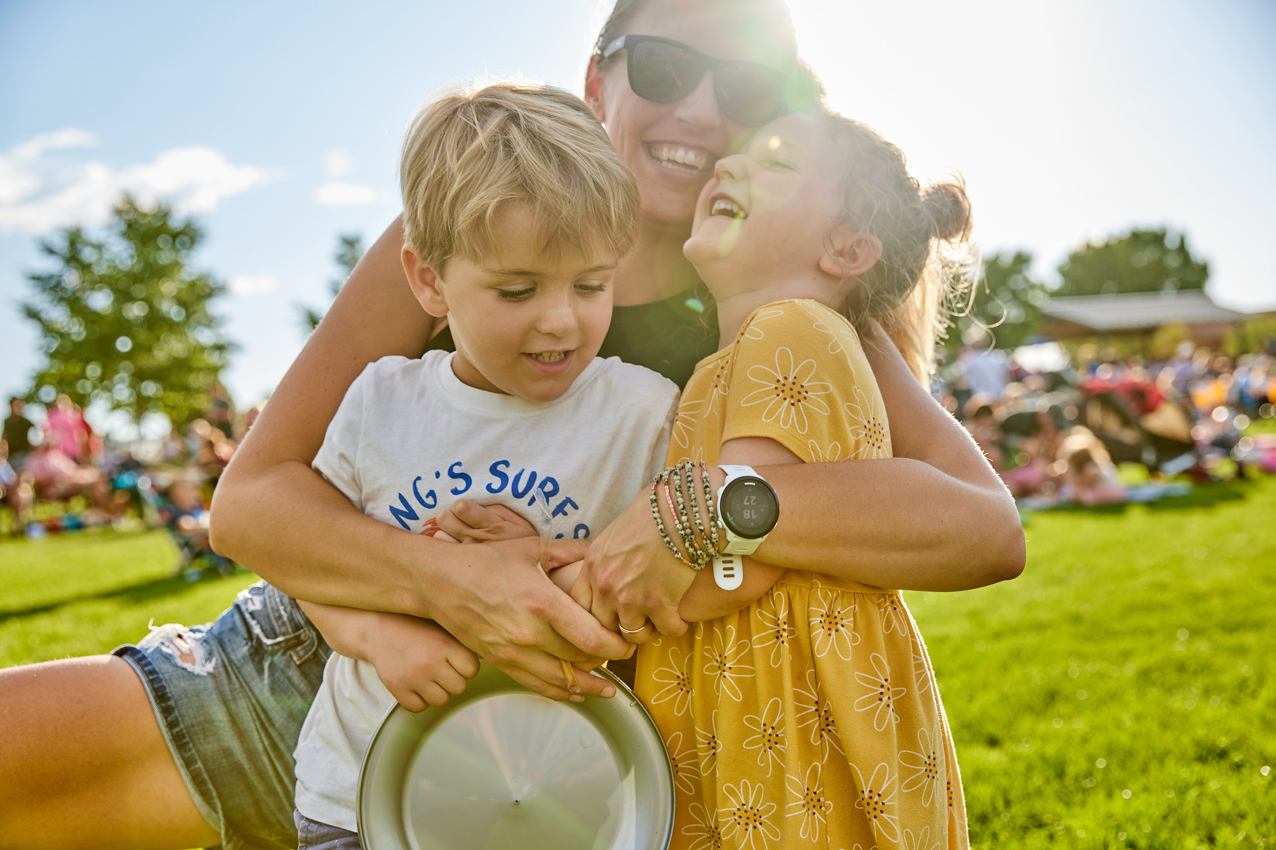 Mom laughing and squeezing two kids at an outdoor concert in Windsor, Colorado- John Robson Lifestyle Photography