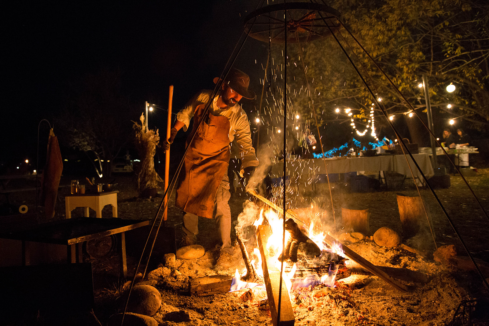 Chef Juan Andres tending a fire at night during an outdoor dinner event - John Robson Photography