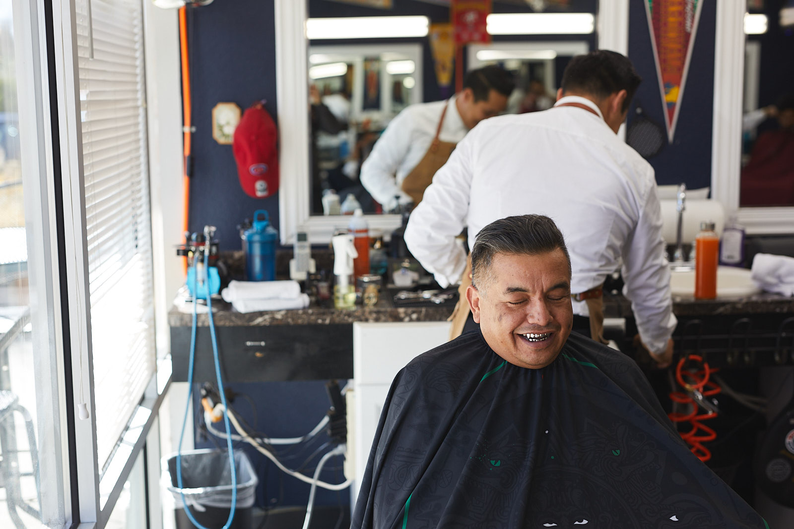 Lifestyle image of a man with gold teeth smiling during a hair cut at a barber shop - John Robson Photography