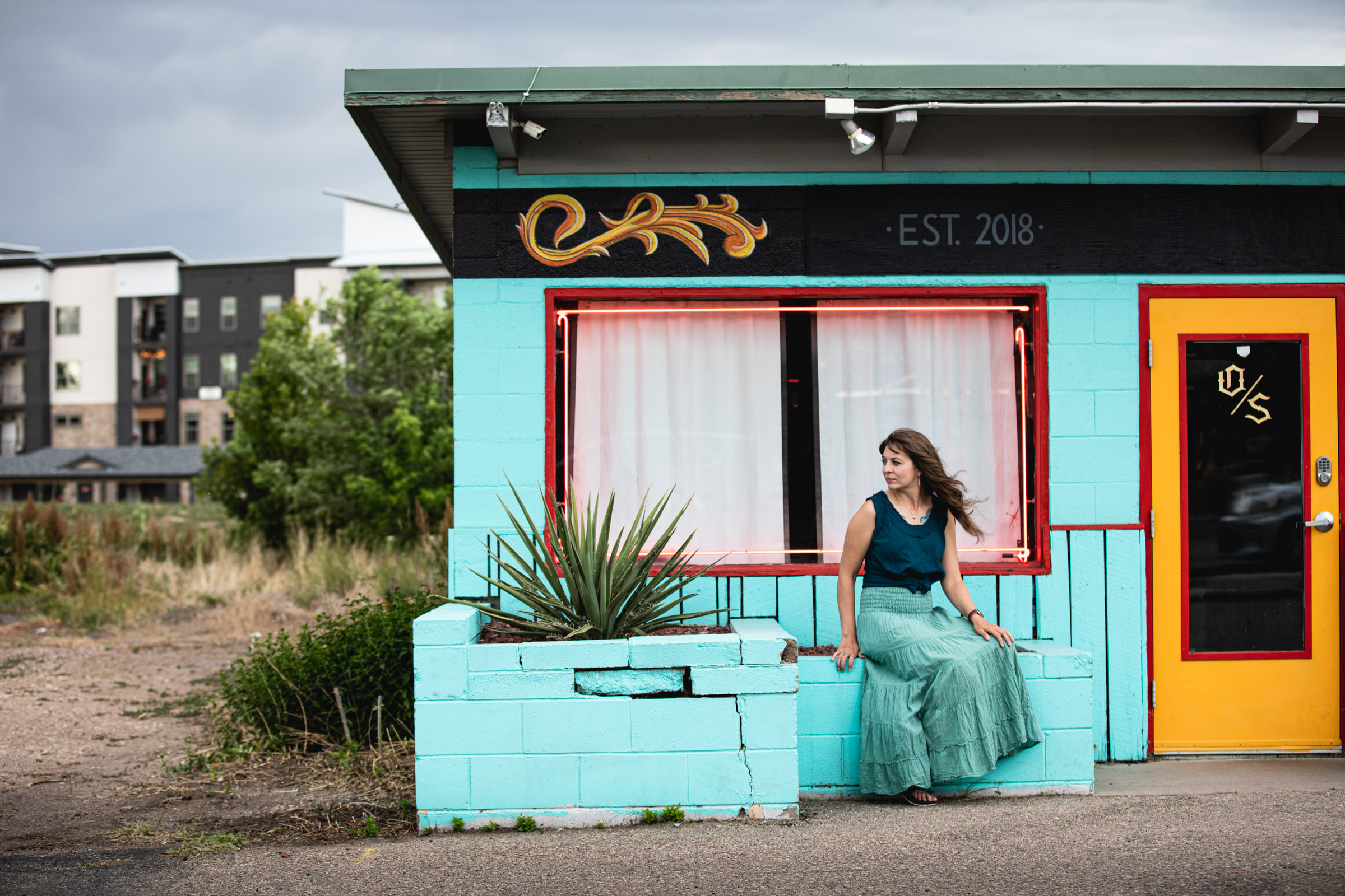 Portrait of a woman sitting on an aqua colored wall in Fort Collins, Colorado