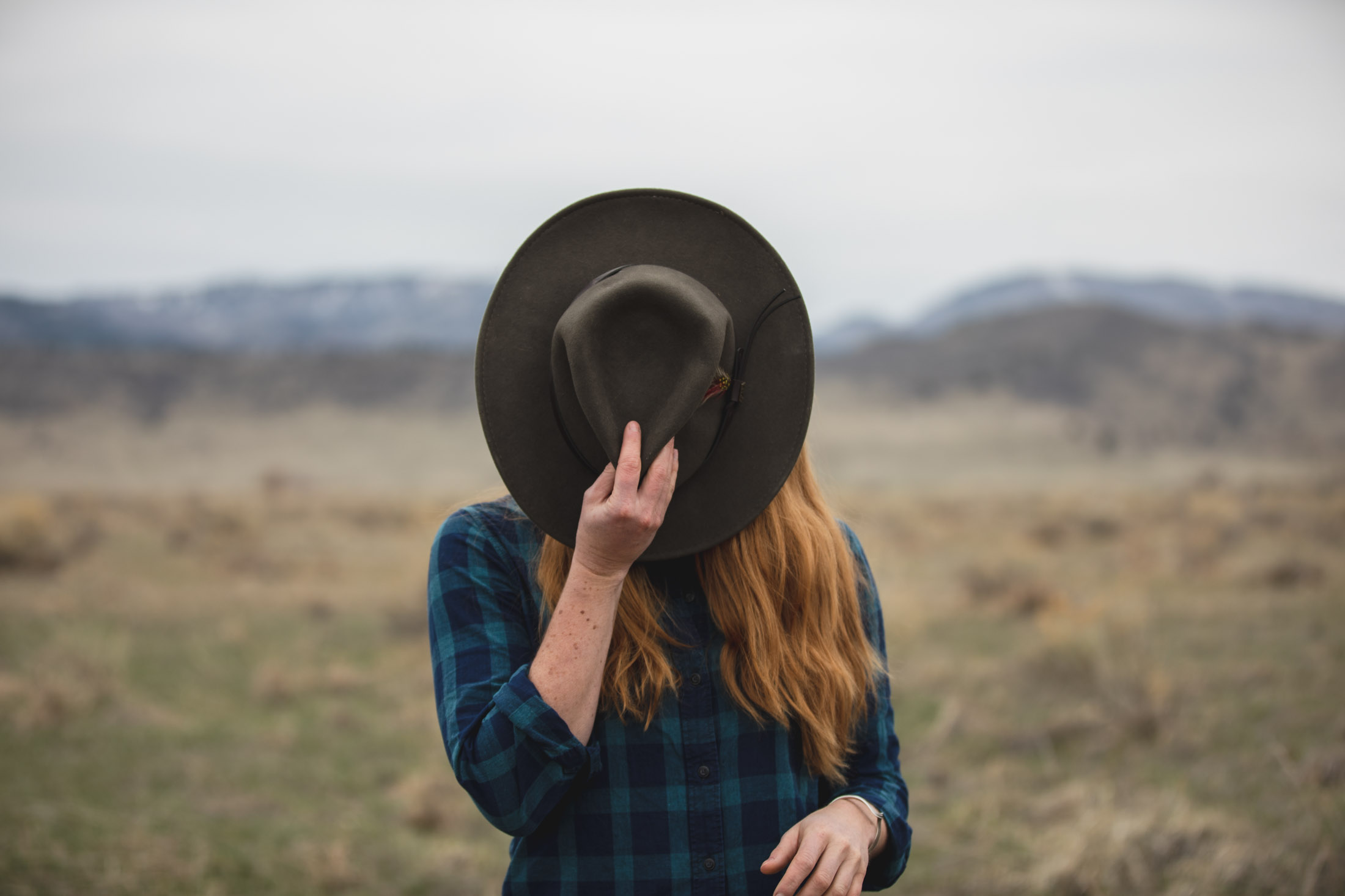 Portrait of an outdoorsy woman standing covering her face with a hat - John Robson Photography