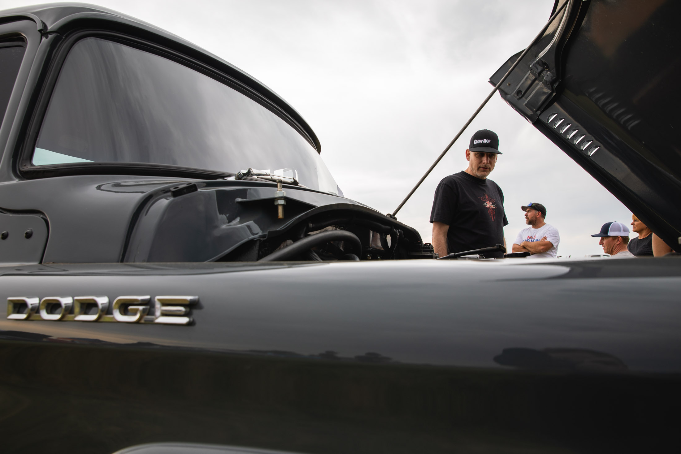 Man looking under the hood of a truck at a car show - John Robson Photography
